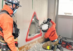 壁を機器で破壊する消防職員の写真
